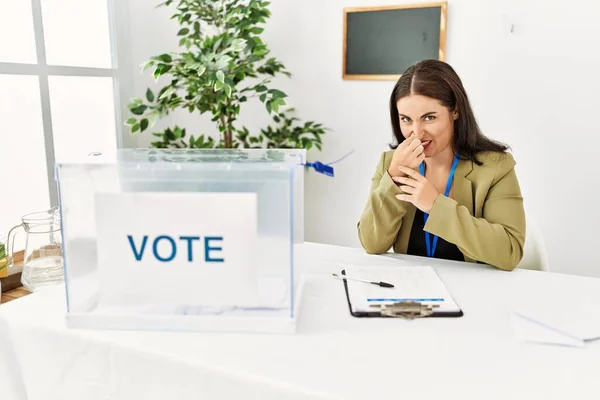 年轻的黑发女人坐在选举桌旁 投票时闻到一股难闻恶心的气味 用手指捂住鼻子屏住呼吸 — 图库照片