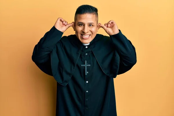 Joven Sacerdote Latino Pie Sobre Fondo Amarillo Sonriendo Tirando Las —  Fotos de Stock