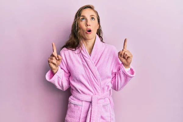 Young Blonde Woman Wearing Bathrobe Amazed Surprised Looking Pointing Fingers — Stock Photo, Image