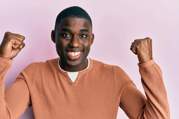 若いアフリカ系アメリカ人の男性は 驚くほどカジュアルな服を着て 腕を上げて目を開いて成功したことに驚いています 勝者のコンセプト — ストック写真