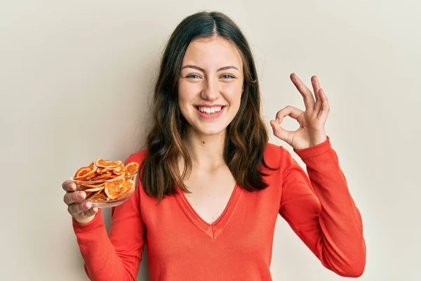 Mujer Morena Joven Sosteniendo Tazón Naranja Seca Haciendo Signo Con — Foto de Stock