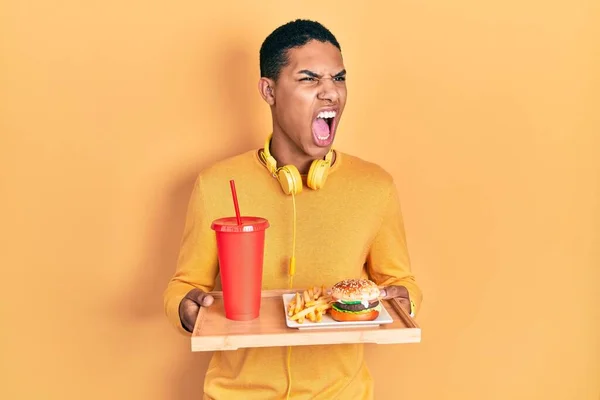 若いアフリカ系アメリカ人の男は 怒りで叫んで イライラし 激怒叫んで おいしい古典的なバーガー怒っていると怒って食べている 怒りと攻撃的な考え方 — ストック写真