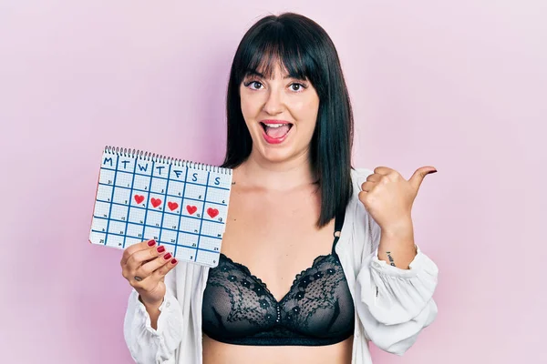 Young Hispanic Woman Holding Menstrual Calendar Wearing Underwear Pointing Thumb — Stock Photo, Image
