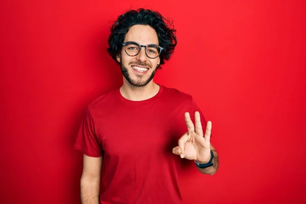 自信を持って幸せな笑顔ながらシャツや眼鏡を身に着けているハンサムなヒスパニック系の男は指の数3で表示し 指摘します — ストック写真