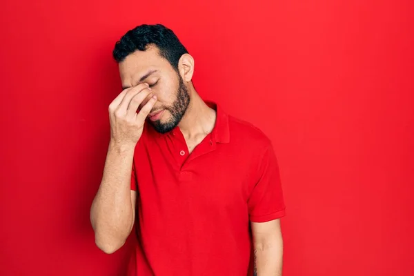 髭を生やしたヒスパニック系の男性は カジュアルな赤いTシャツを着て疲れ鼻や目をこすり疲労や頭痛を感じている ストレスとフラストレーションの概念 — ストック写真