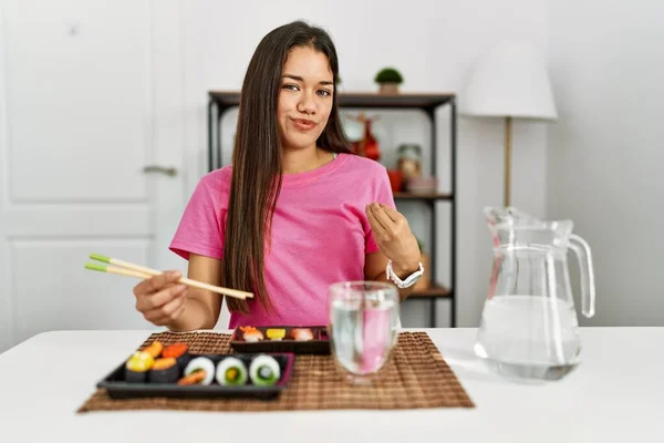 Joven Morena Comiendo Sushi Usando Palillos Haciendo Gesto Dinero Con —  Fotos de Stock