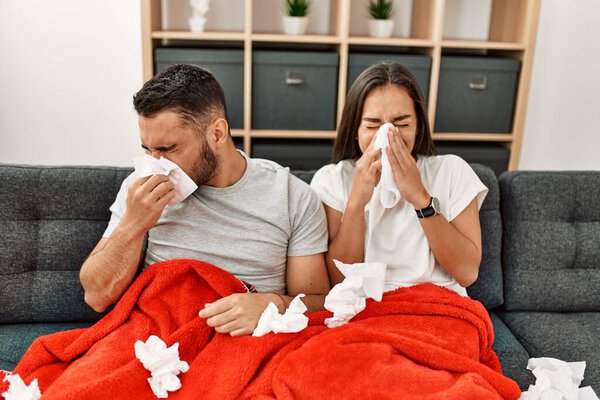Young latin ill couple using napkin sititng on the sofa at home.