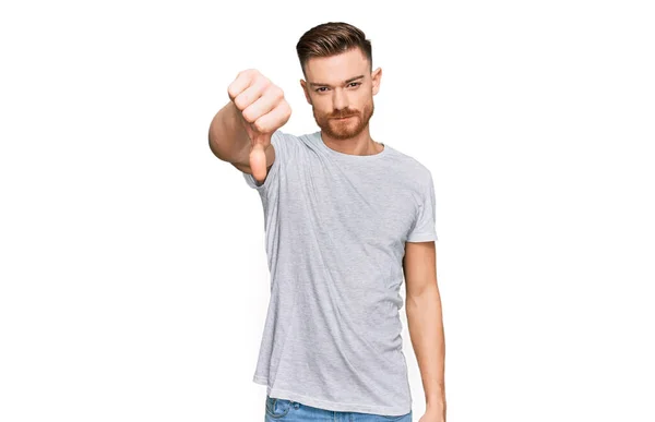 カジュアルなグレーのTシャツを着た若い赤毛の男は 親指を下にジェスチャーで拒絶と否定を示す不満と怒りを見ています 悪い表現 — ストック写真