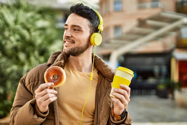 若いヒスパニック系の男が街でヘッドフォンを使用して朝食を持っています — ストック写真