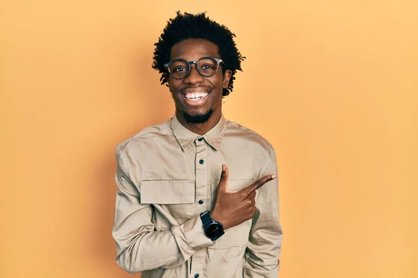 若いアフリカ系アメリカ人の男性は 笑顔で陽気なカジュアルな服と眼鏡を手と指で顔に幸せと自然な表情で側面まで指しています — ストック写真