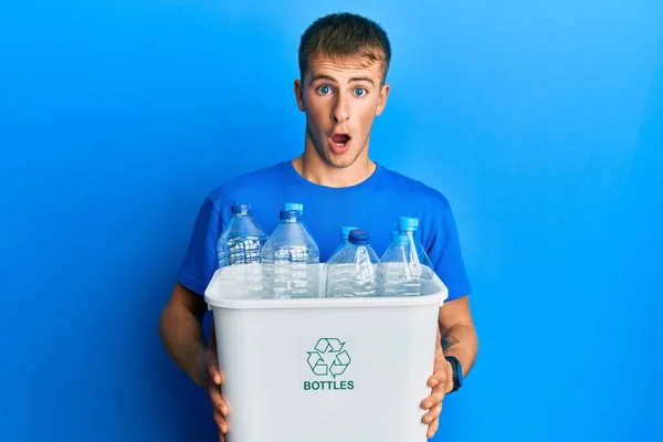プラスチックボトルでリサイクルゴミ入れを保持している若い白人男性は恐れていると驚きと驚きの表情でショックを受けました 恐怖と興奮した顔 — ストック写真