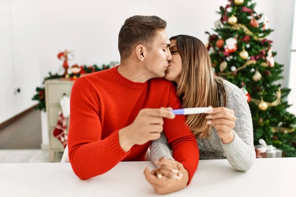 年轻夫妇亲吻和举行怀孕测试 坐在家里的桌子上 — 图库照片