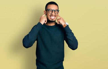 Genç Afro-Amerikan adam gündelik kıyafetler giyip kulaklarını parmaklarıyla kapatıyor ve yüksek sesli müzik sesi için rahatsız edici bir ifade takınıyor. sağır kavramı. 