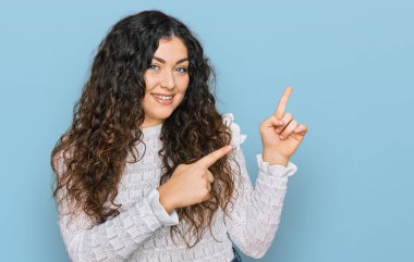 Gündelik kıyafetler giyen, gülümseyen ve kameraya bakan genç İspanyol kız iki eliyle ve parmaklarıyla kenarı işaret ediyor.. 