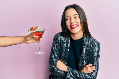 Seksi parti ceketi giyen ve İspanyol kollu genç bir kız kollarını kavuşturup kameraya bakarken gülümseyen bir kokteyl sunuyor. pozitif kişi. 