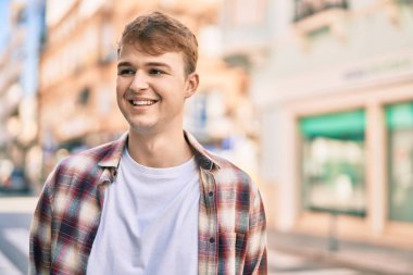 Genç beyaz adam gülümseyerek şehirde mutlu mesut duruyor..