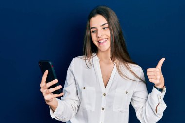 Genç esmer kız masada oturmuş gülümsüyor, gülümsüyor ve olumlu bakıyor, başparmağını kaldırıyor ve işaret veriyor. 