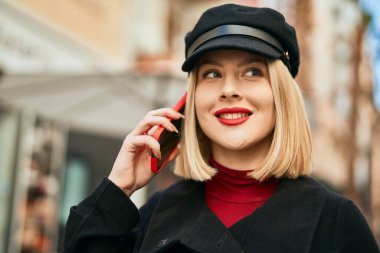 Genç sarışın kadın gülümsüyor. Şehirdeki akıllı telefondan konuşuyor..