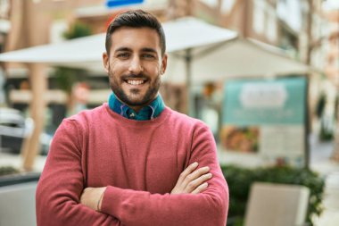 Kollarını kavuşturup gülümseyen genç İspanyol adam şehirde mutlu bir şekilde duruyor..