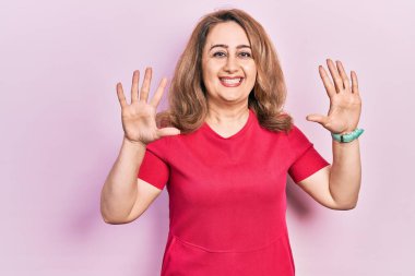 Orta yaşlı, beyaz, günlük kıyafetler giyen bir kadın on numarayı gösterip işaret ederken kendinden emin ve mutlu bir şekilde gülümsüyor.. 