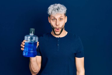 Modern boyalı saçları olan genç İspanyol bir adam taze nefes için gargara tutuyor. Korkmuş ve şaşırmış bir şekilde ağzı açık, inançsız bir yüz. 