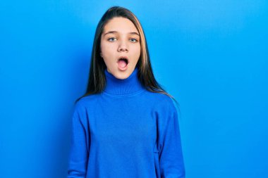 Young brunette girl wearing turtleneck sweater afraid and shocked with surprise and amazed expression, fear and excited face. 