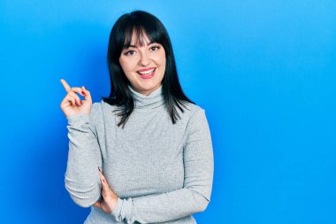 Yüzünde kocaman bir gülümseme olan, gündelik kıyafetler giyen genç İspanyol kadın, kameraya el ve parmak ile bakıyor.. 