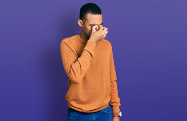 Genç Afro-Amerikan adam günlük kıyafetler giyip yorgun burnu ve gözleri ovuşturup yorgun ve baş ağrısı çekiyor. Stres ve hüsran kavramı. 