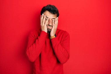 Sakallı, sıradan kırmızı kazak giyen, yüzü, depresyonu ve üzüntüyü örten yakışıklı bir adam. 