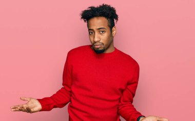 Young african american man with beard wearing casual winter sweater clueless and confused with open arms, no idea concept. 