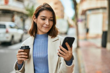 Genç İspanyol kadın akıllı telefon kullanıyor ve şehirde kahve içiyor..