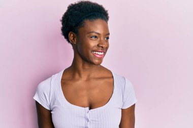 Afro-Amerikalı genç bir kız, günlük giysiler giymiş, rahat bir görünüm takınıyor, doğal bir yüz ifadesi ve kendine güvenen bir gülümsemeyle poz veriyor.. 