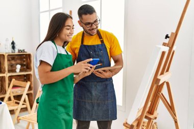 Sanat stüdyosunda akıllı telefon kullanarak mutlu bir şekilde gülümseyen genç İspanyol çift..