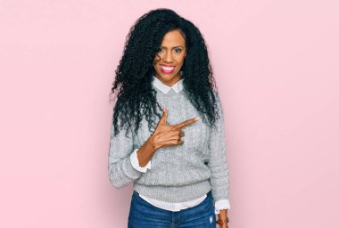 Orta yaşlı Afro-Amerikalı kadın, günlük giysiler giymiş, neşeli, yüzünde bir gülümsemeyle, mutlu ve doğal bir ifadeyle elini ve parmağını kaldırmış. 