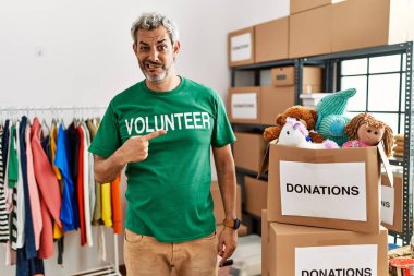 Orta yaşlı İspanyol bir adam bağışlarda gönüllü tişört giyer endişeli ve gergin bir şekilde işaret eder. 