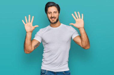 Günlük beyaz tişört giyen genç İspanyol adam on numarayı gösterip işaret ederken kendinden emin ve mutlu gülümsüyor.. 