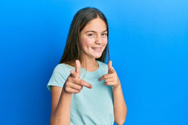 Gayri resmi beyaz tişört giyen güzel esmer kız mutlu ve komik yüzüyle kamerayı işaret ediyor. iyi enerji ve titreşimler. 