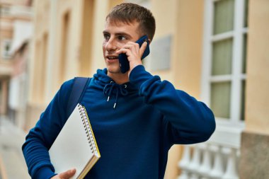 Üniversitede elinde not defteriyle konuşan sarışın genç bir öğrenci..