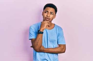 Genç Afro-Amerikalı bir adam günlük mavi tişörtler giyiyor ve elleri çenesinde soru sormayı düşünüyor, düşünceli bir ifade. Düşünceli bir yüzle gülümsüyor. şüphe kavramı. 