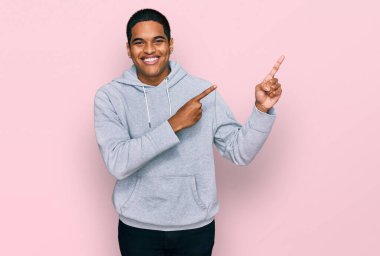 Genç, yakışıklı, sıradan bir kazak giyen, gülümseyen ve kameraya bakıp iki elini ve parmağını yana doğru gösteren bir adam.. 