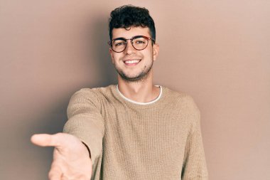 Gündelik giysiler ve gözlük takan genç İspanyol adam gülümseyen, yardım eli uzatan ve kabul gören biri.. 