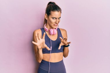 Spor kıyafetleri giyen ve kulaklık takan genç ve güzel bir kadın tiksindirici tepki verdiği için mutsuz ve korkmuş bir ifade takınıyor. Eller havada. 