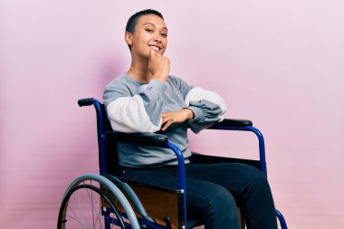 Tekerlekli sandalyede oturan güzel İspanyol kadın kameraya kollarını kavuşturup gülümseyerek ve çenesini kaldırarak bakıyor. Olumlu düşünmek. 