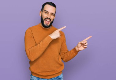 Sakallı genç adam, sıradan bir kazak giyiyor gülümsüyor ve kameraya bakıyor.. 