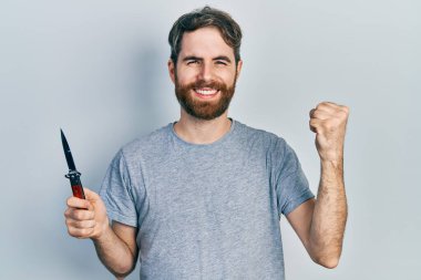 Sakallı, elinde çakı olan beyaz bir adam gururla bağırıyor, zaferi kutluyor ve başarıyı kollarını kaldırarak kutluyor. 