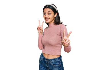 Gündelik kıyafetler giyen genç İspanyol kız kameraya bakıp zafer işareti yaparken parmaklarını gösteriyor. İki numara.. 