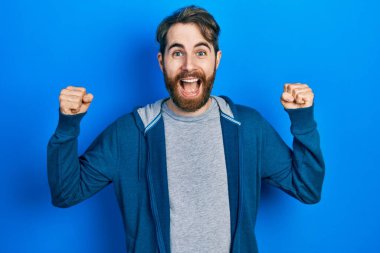 Sakallı, sıradan bir kazak giyen beyaz bir adam kolları havada ve gözleri açık bir şekilde başarıyı kutluyor ve şaşırıyor. Kazanan konsept. 