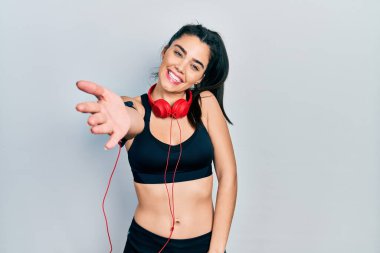 Spor kıyafetleri giyen, kulaklık takan, dostça gülümseyen ve selamlaşan İspanyol bir kız. başarılı iş. 