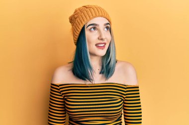 Yün şapka takan, yüzünde gülümsemeyle yan yana bakan genç modern bir kız, doğal bir ifade. Kendinden emin gülen. 