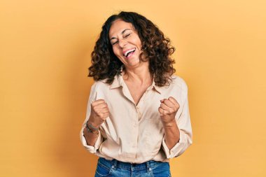 Orta yaşlı İspanyol kadın gündelik giysiler giyiyor başarı için heyecanlı kolları havada ve gözleri kapalı zaferi kutlarken gülümsüyor. Kazanan konsept. 